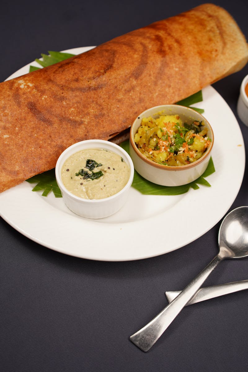 Crispy dosa served with coconut chutney, vegetable curry, and sambar on a black background.